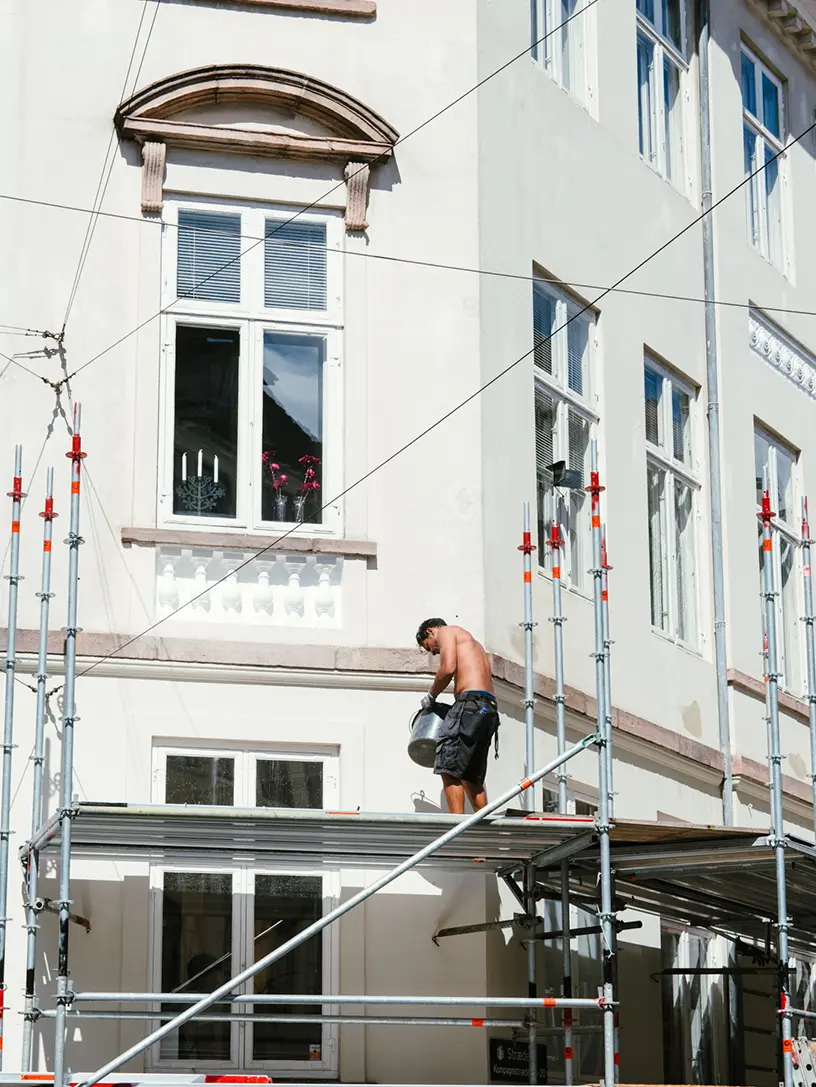 En mand på et stillads foran en bygning er ved at færdiggøre håndværkertilbud på huset.