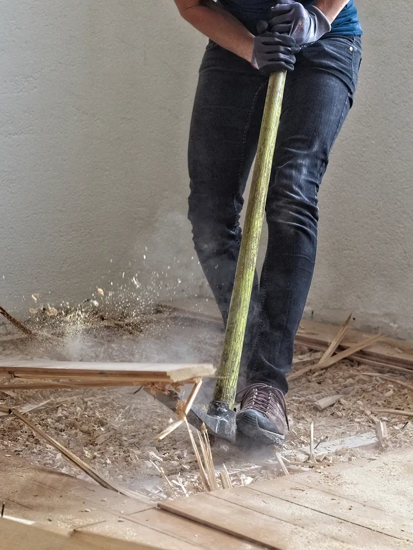En kvinde bruger en hammer til at slibe et trægulv som en del af et håndværkertilbud til sit hus.