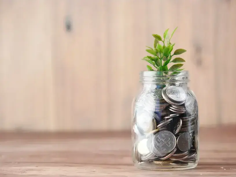 En glaskrukke med mønter og en plante brugt som visuel fremstilling til beregning af boliglån.